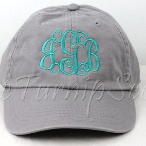 May include: A gray baseball cap with a teal monogram embroidered on the front.