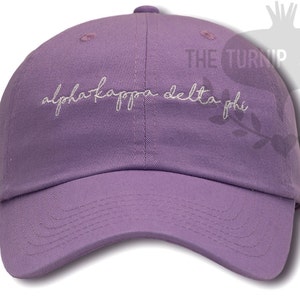 May include: A purple baseball cap with the text "alpha kappa delta phi" embroidered in white on the front.
