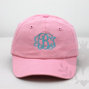 May include: A pink baseball cap with a turquoise embroidered monogram. The monogram is a stylized "J.B."