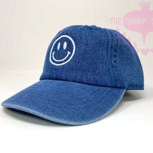 May include: A blue denim baseball cap with a white embroidered smiley face.
