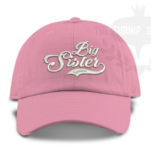 May include: Pink baseball cap with white embroidered text that reads "Big Sister".