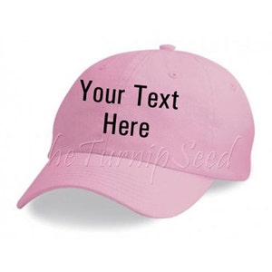May include: A light pink baseball cap with a curved brim. The text "Your Text Here" is printed in black on the front. The Turnip Seed logo is printed in a light pink script on the bottom of the cap.
