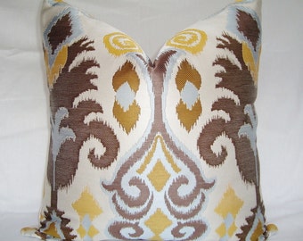 May include: Decorative throw pillow with a cream background and an intricate pattern in brown, yellow, and light blue. The design features stylized floral and geometric shapes, creating a textured appearance. The pillow is square and appears to be made of a woven fabric.