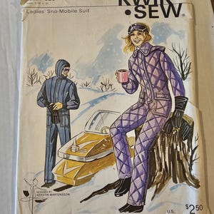 May include: Vintage Kwik Sew pattern 320 for a Ladies' Sno-Mobile Suit. The illustration shows a woman in a purple quilted snowsuit with black gloves and boots, and a man in a blue snowsuit. The pattern includes sizes S, M, L, and XL.