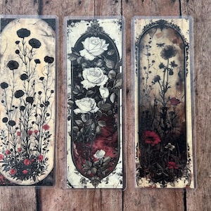 May include: Three bookmarks with floral designs. The first bookmark features black flowers on a white background. The second bookmark features white roses on a red and white background. The third bookmark features red flowers on a brown and white background.