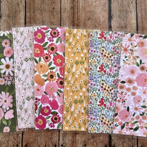 May include: A collection of floral patterned bookmarks in various designs. The bookmarks feature colorful flowers on backgrounds of green, pink, yellow, and white. Each bookmark is encased in a clear plastic sleeve.