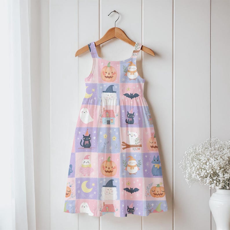 K&ouml;nnte beinhalten: Ein &auml;rmelloses Kleid mit einem Karomuster aus pastellrosa und hellvioletten Quadraten. Der Druck zeigt Illustrationen von orangefarbenen K&uuml;rbissen, schwarzen Katzen, wei&szlig;en Geistern, Flederm&auml;usen, gelben Mondsicheln und kleinen H&auml;usern.