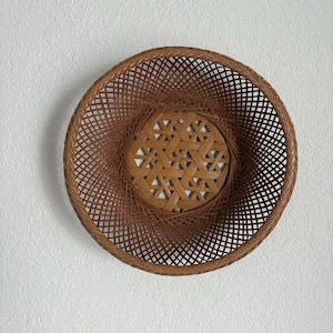 May include: A round, woven basket with a spiral design. The basket is made of brown bamboo and features a central, patterned base. The open weave allows light to pass through, creating a decorative effect. This basket is suitable for home decor.