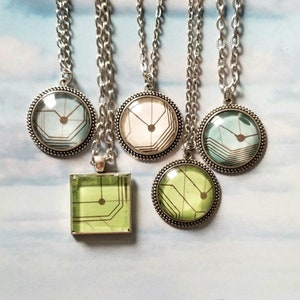 May include: Five silver necklaces with different coloured glass pendants featuring a circuit board design. The pendants are round except for one, which is square.