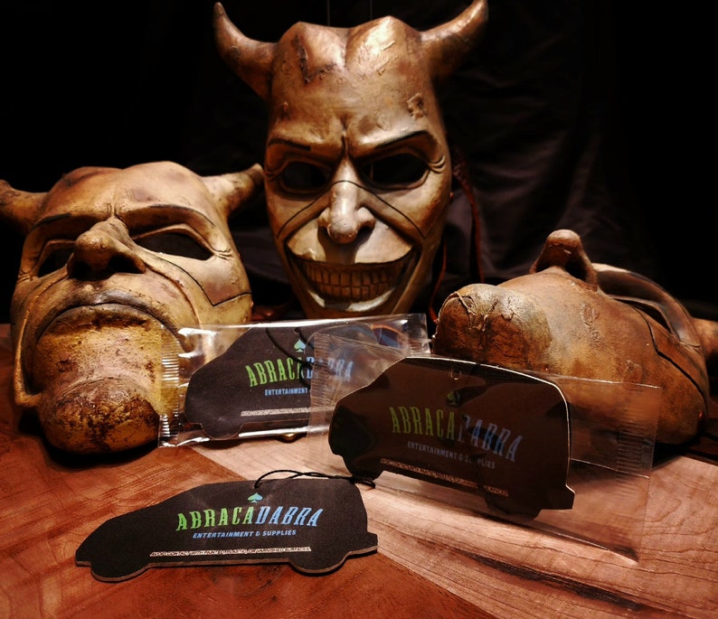 May include: Three brown, demonic-looking masks with horns and exaggerated features.  Three black car air fresheners with the text "ABRACADABRA ENTERTAINMENT & SUPPLIES" in green and blue lettering.