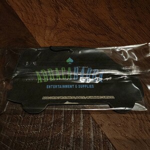 May include: A black car air freshener with the text "Remarkable" in green and blue letters. The text "Entertainment & Supplies" is printed below the logo. The air freshener is packaged in a clear plastic bag.