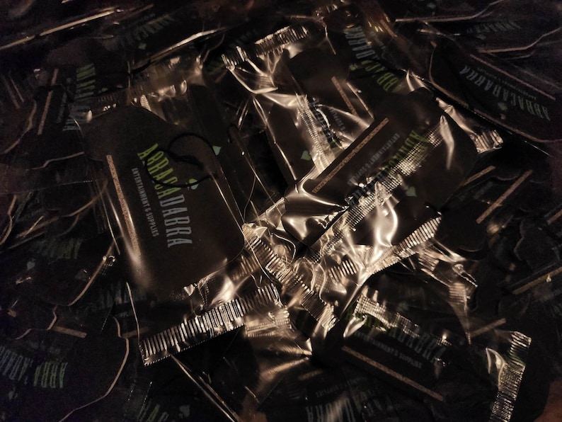 May include: A pile of black and green car air fresheners with the text "Abracadabra Entertainment & Supplies" on them.