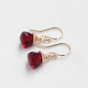 May include: A pair of earrings with red gemstone drops wrapped in gold wire.