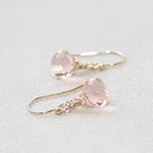 May include: A pair of delicate earrings featuring pink quartz gemstones wrapped in gold wire. The earrings have a simple, elegant design and are perfect for everyday wear.