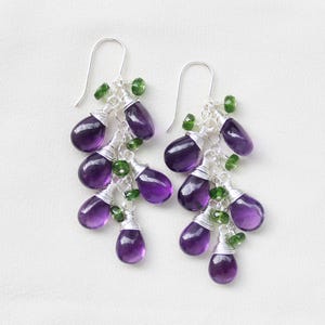 Könnte beinhalten: Amethyst- und grüner Edelstein-Ohrringe mit silbernem Drahtgeflecht. Die Ohrringe haben mehrere tropfenförmige Edelsteine.