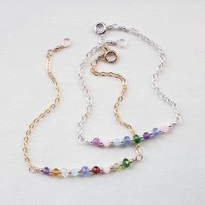 May include: Two delicate necklaces with colorful gemstone beads. One necklace is gold-toned, the other silver-toned. Each features a chain with a row of small, round beads in various colors, including pink, purple, green, and blue. The necklaces are displayed on a white surface.