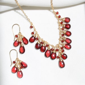 K&ouml;nnte beinhalten: Ein goldenes Halsketten- und Ohrring-Set mit roten Edelstein-Tropfen. Die Halskette hat ein kaskadierendes Design mit mehreren roten Edelstein-Tropfen, die an einer goldenen Kette h&auml;ngen. Die Ohrringe sind im H&auml;nge-Stil mit mehreren roten Edelstein-Tropfen, die an goldenen Haken h&auml;ngen.