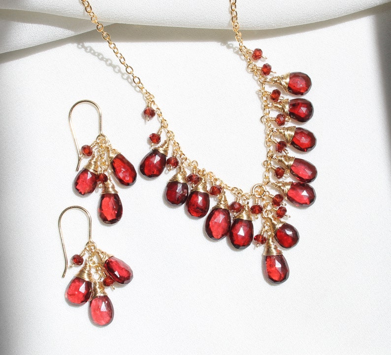 K&ouml;nnte beinhalten: Ein goldenes Halsketten- und Ohrring-Set mit roten Edelstein-Tropfen. Die Halskette hat ein kaskadierendes Design mit mehreren roten Edelstein-Tropfen, die an einer goldenen Kette h&auml;ngen. Die Ohrringe sind im H&auml;nge-Stil mit mehreren roten Edelstein-Tropfen, die an goldenen Haken h&auml;ngen.