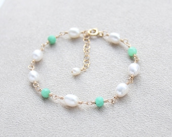 Könnte beinhalten: Ein zartes Armband mit abwechselnd weißen, ovalen Süßwasserperlen und kleinen, runden, mintgrünen Perlen, die mit einem dünnen goldfarbenen Draht verbunden sind. Das Schmuckstück hat eine goldfarbene Verlängerungskette mit einer einzelnen Perle.