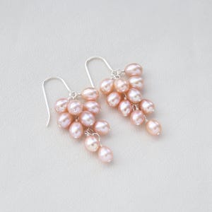 May include: A pair of silver dangle earrings with a cluster of pink freshwater pearls. The pearls are arranged in a cascading design, creating a delicate and feminine look.
