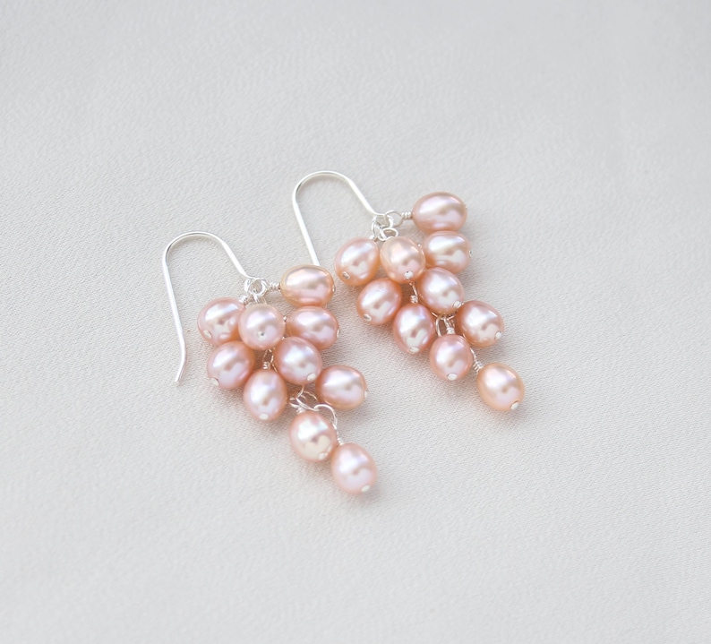 May include: A pair of silver dangle earrings with a cluster of pink freshwater pearls. The pearls are arranged in a cascading design, creating a delicate and feminine look.