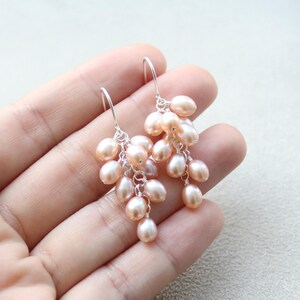 May include: A pair of dangle earrings with a cluster of blush pink freshwater pearls hanging from silver hooks.
