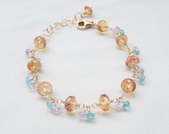 Könnte beinhalten: Ein goldfarbenes Kettenarmband mit facettierten bernsteinfarbenen Perlen, durchsetzt mit kleineren, herabhängenden hellblauen und blass lavendelfarbenen Edelsteinakzenten. Das Armband hat einen goldenen Karabinerverschluss und eine verstellbare Kette.
