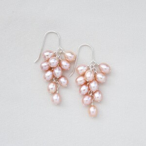 May include: A pair of silver earrings with a cluster of pink freshwater pearls hanging from each earring.