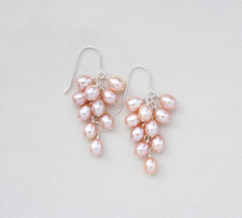 May include: A pair of silver earrings with a cluster of pink freshwater pearls hanging from each earring.