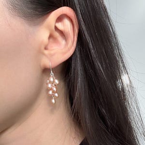 May include: A pair of dangle earrings featuring a cluster of blush pink freshwater pearls hanging from a silver hook.