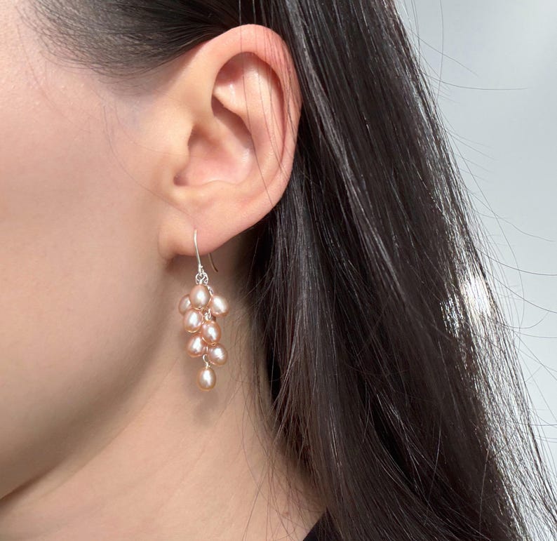 May include: A pair of dangle earrings featuring a cluster of blush pink freshwater pearls hanging from a silver hook.