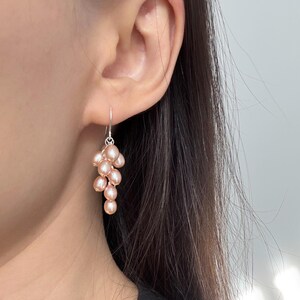May include: A pair of dangle earrings featuring a cluster of blush-colored pearls hanging from a silver hook.