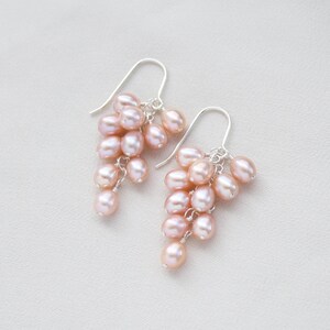 May include: A pair of dangle earrings with a cluster of pink freshwater pearls hanging from silver hooks.