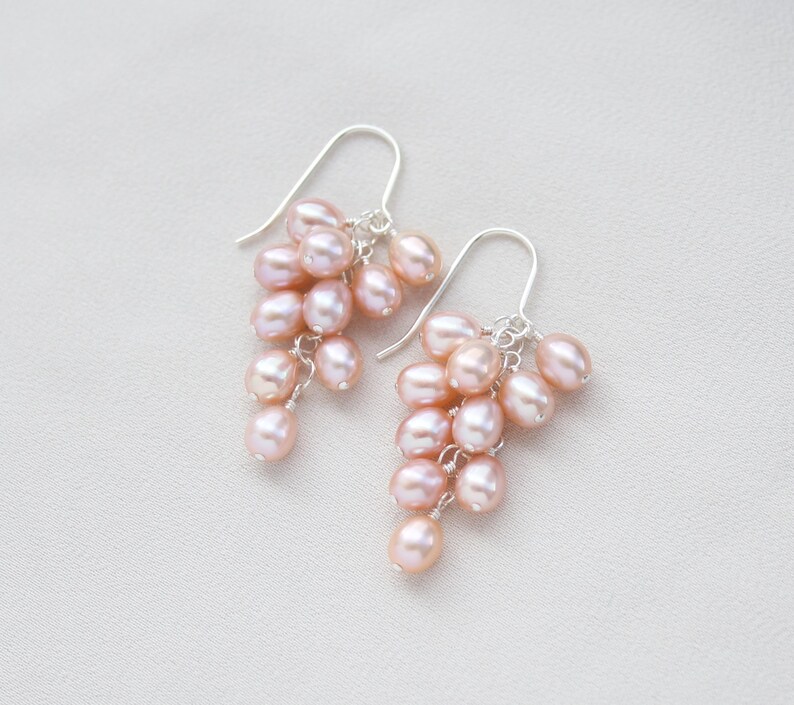 May include: A pair of dangle earrings with a cluster of pink freshwater pearls hanging from silver hooks.