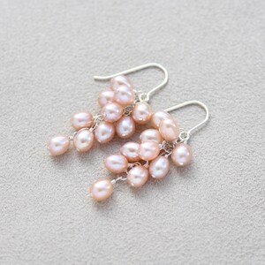 May include: A pair of dangle earrings with a cluster of blush pink pearls hanging from silver hooks.