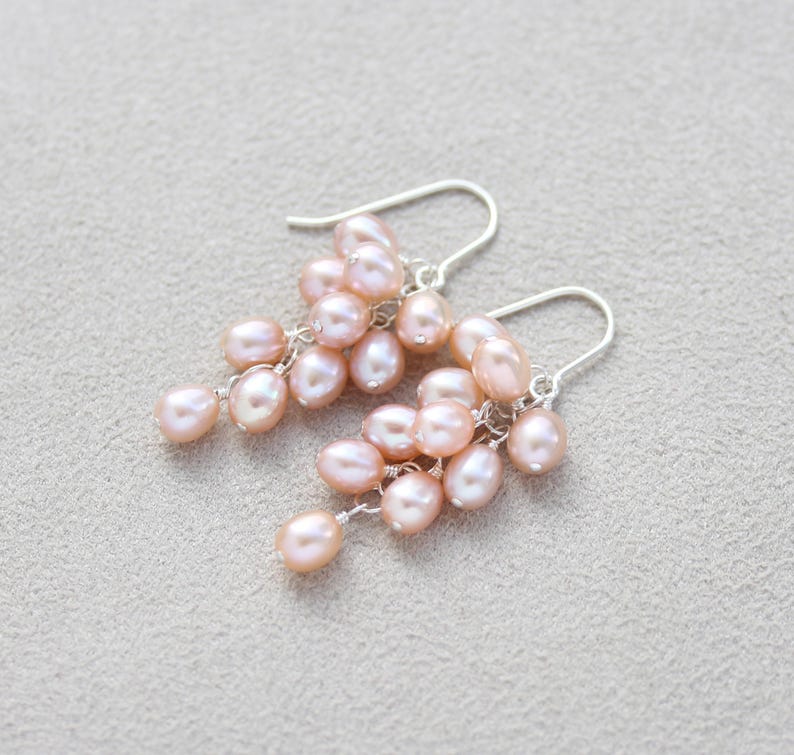May include: A pair of dangle earrings with a cluster of blush pink pearls hanging from silver hooks.