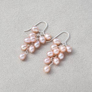 May include: A pair of dangle earrings with a cluster of pink pearls hanging from silver hooks.
