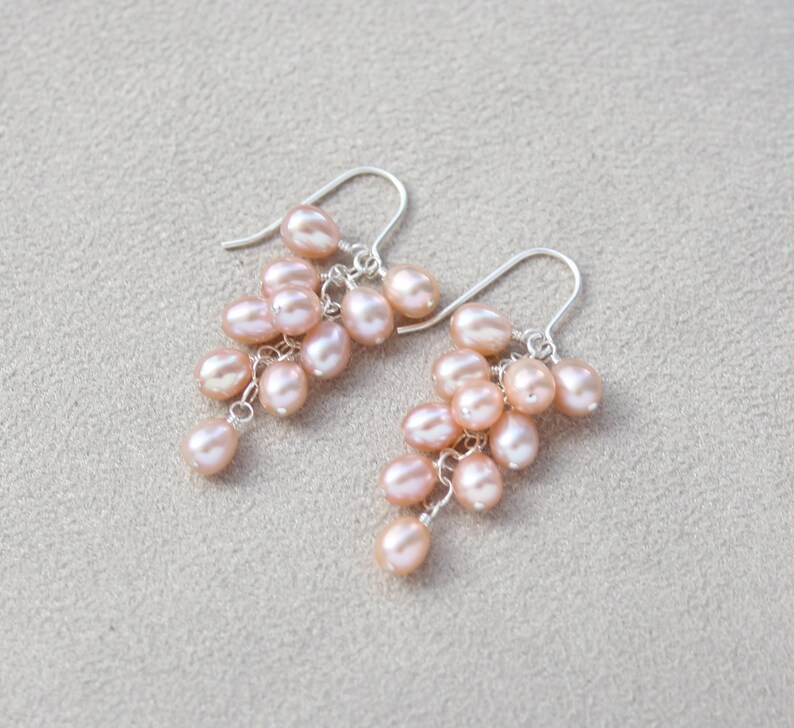 May include: A pair of dangle earrings with a cluster of pink pearls hanging from silver hooks.