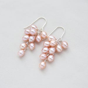 May include: A pair of silver dangle earrings with a cluster of pink freshwater pearls. The pearls are arranged in a cascading design, creating a delicate and feminine look.
