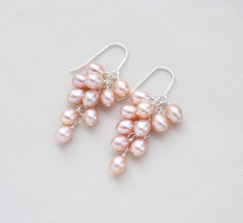 May include: A pair of silver dangle earrings with a cluster of pink freshwater pearls. The pearls are arranged in a cascading design, creating a delicate and feminine look.