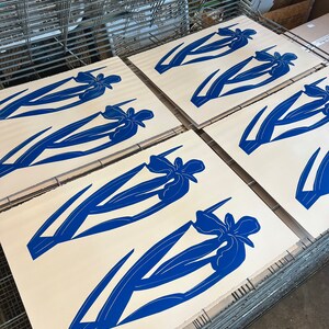Pode incluir: Cinco telas brancas com impress&otilde;es de flores de &iacute;ris azuis em uma prensa de serigrafia.