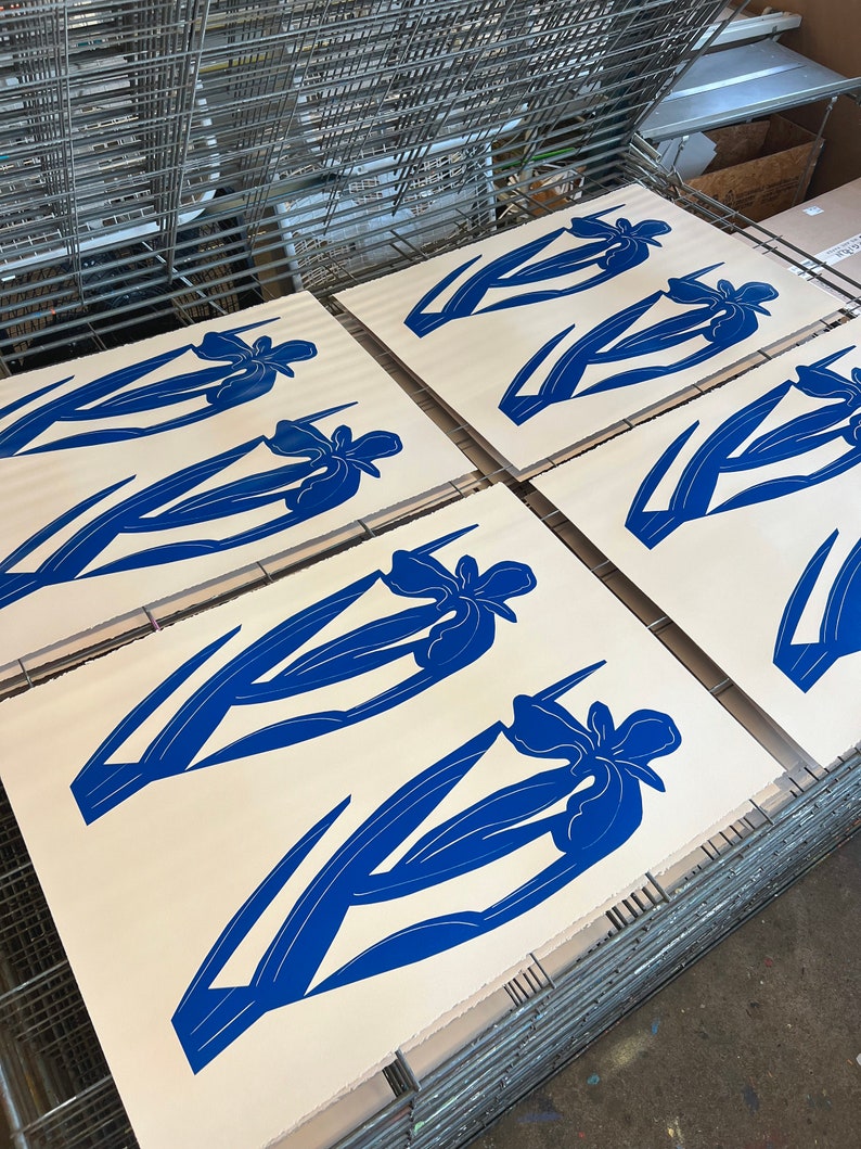 Pode incluir: Cinco telas brancas com impress&otilde;es de flores de &iacute;ris azuis em uma prensa de serigrafia.