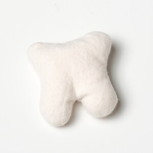May include: A plush, off-white tooth-shaped pillow. The pillow has a rounded, three-lobed design, with a textured, soft surface. The item is designed to resemble a molar and is likely a decorative or novelty item.