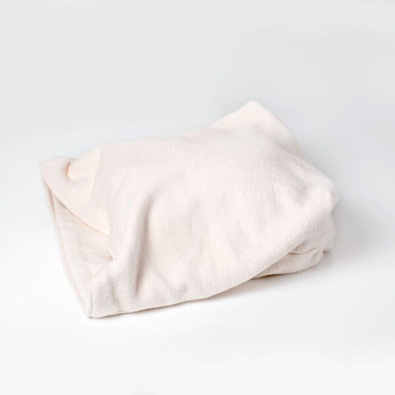 Image shows a partially open organic cat bed. It is white/ natural cotton.  The outside white layer is thick fuzzy organic sherpa cotton.  The inner layer is a smoother organic cotton fleece.  Background is white too.  Natural Organic Cat Beds.
