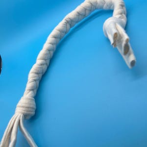 May include: A white, braided rope toy for dogs, with a knotted end and a flared, hollow end. The toy is made of a soft, fuzzy material and is set against a bright blue background.