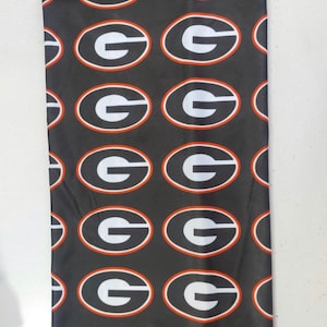 May include: Black neck gaiter with a repeating pattern of white 'G's inside orange circles.