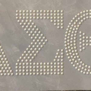 May include: White pearl-like beads arranged in the shape of the Greek letters Delta, Sigma, and Theta.