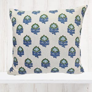 Könnte beinhalten: Quadratisches Zierkissen mit einem sich wiederholenden Blumenmuster in Blau- und Grüntönen auf cremefarbenem Hintergrund. Das Kissen besteht aus einem strukturierten Stoff und dient der Heimdekoration.