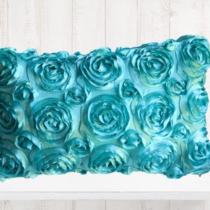May include: Teal blue decorative throw pillow with a 3D rose pattern.