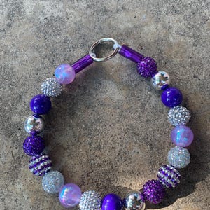 May include: A purple and silver beaded dog collar with a silver clasp. The beads are various sizes and shapes, including round, square, and star-shaped.